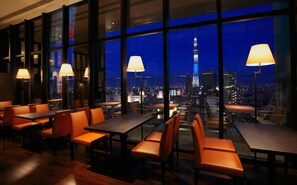 A restaurant with tables and chairs, large windows, and a view of a cityscape including a tower. - The Gate Hotel Kaminarimon by Hulic (Tokyo)
