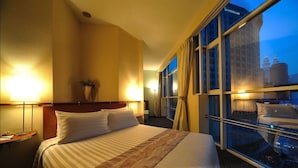A hotel room with a large bed, a nightstand, a lamp, and a window with a city view. - Alpha Genesis Hotel Kuala Lumpur (Kuala Lumpur)
