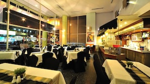 A restaurant with multiple dining tables, black chairs, and a bar area. - Alpha Genesis Hotel Kuala Lumpur (Kuala Lumpur)