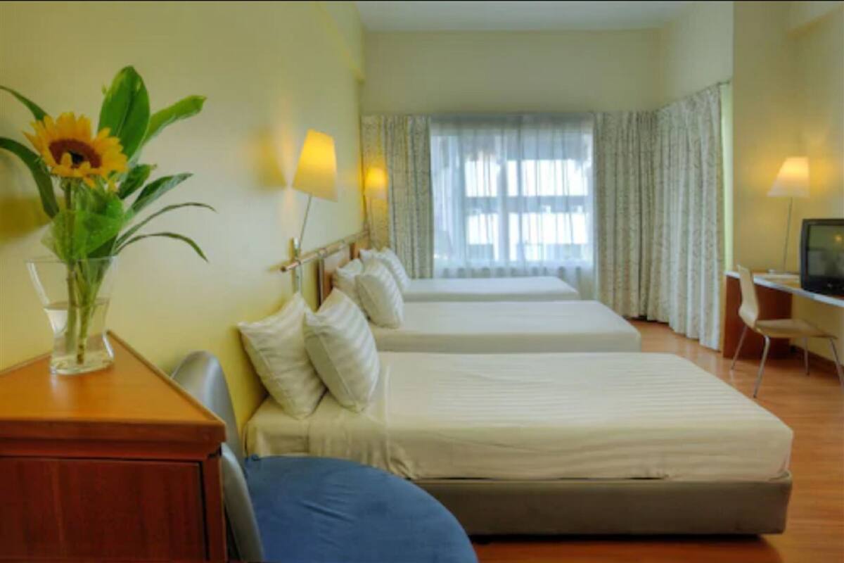 A hotel room with two beds, a desk with a lamp, a TV, and a window with curtains.