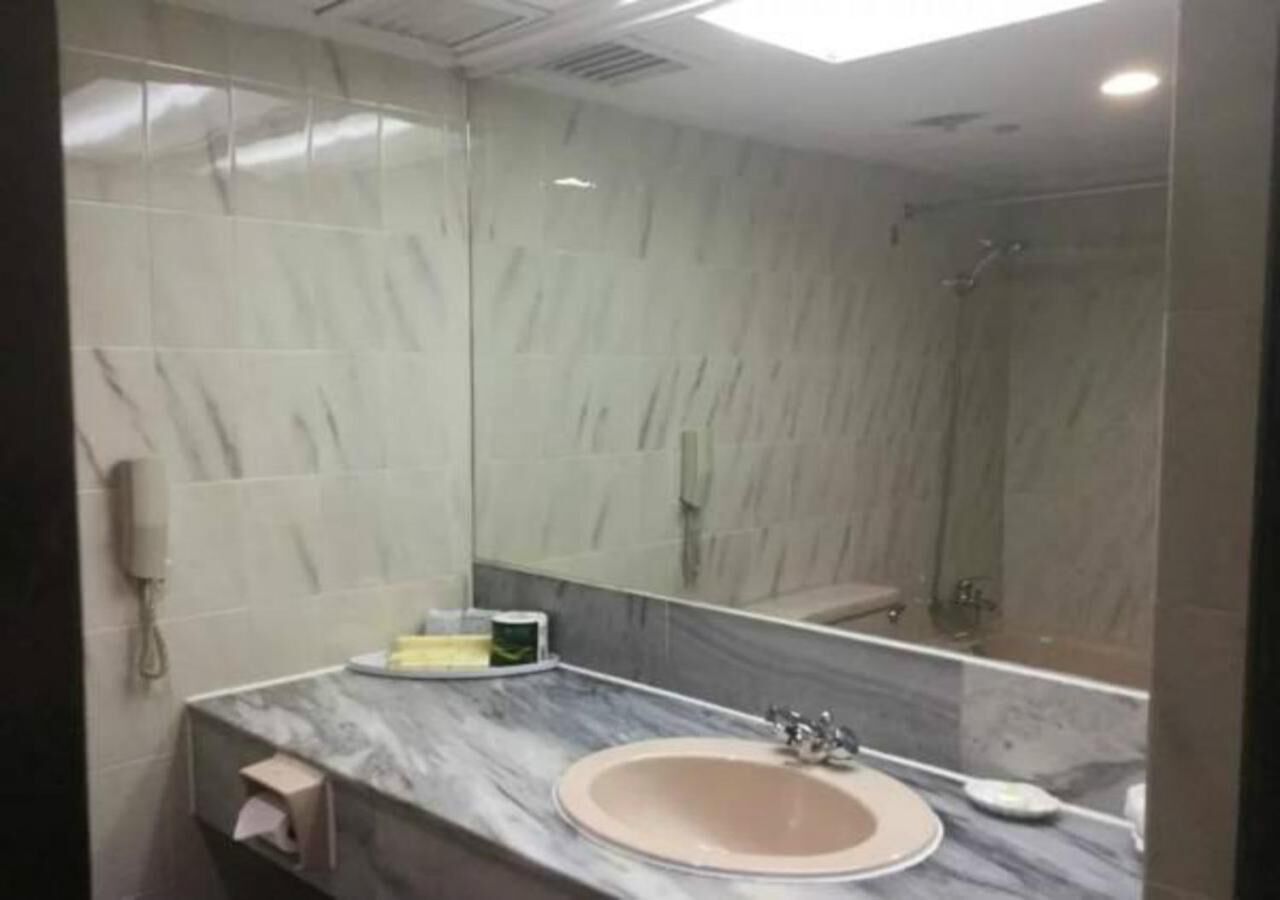 A bathroom with a marble countertop, a sink, a mirror, and a shower area.