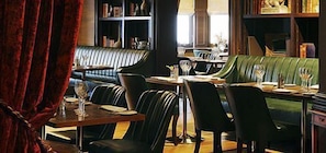 Un restaurante con cabinas de cuero, una mesa de madera y una estantería al fondo.