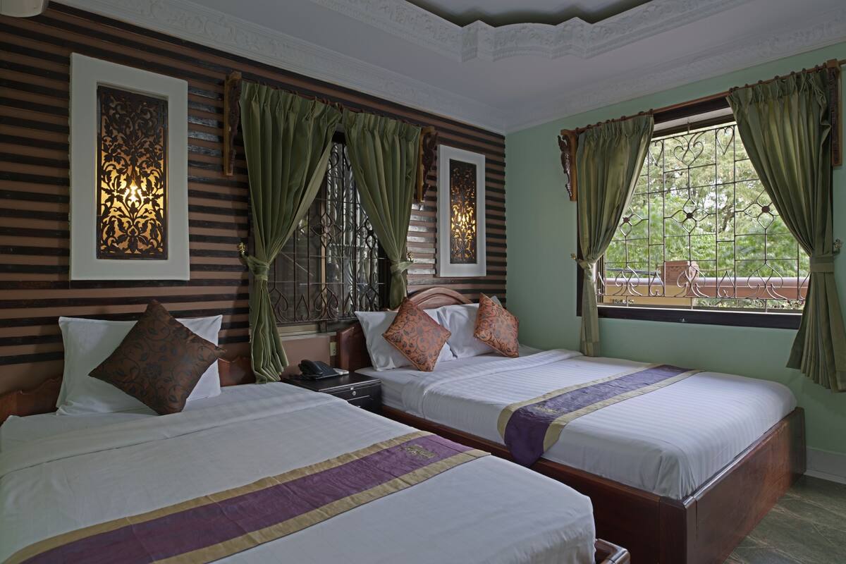 A hotel room with two beds, green curtains, and decorative wall panels.