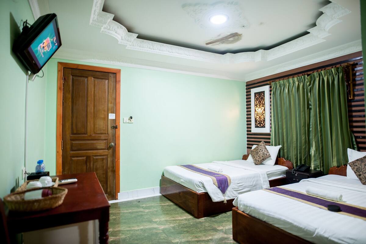 A hotel room with two single beds, a television on the wall, a wooden door, and a green curtain.
