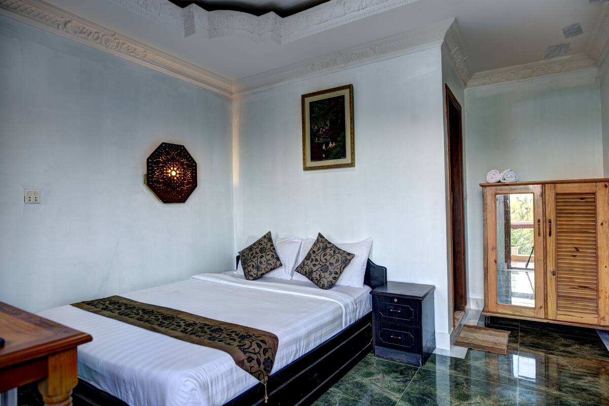 A bedroom with a bed, a nightstand, a wooden cabinet, and a wall-mounted decorative piece.