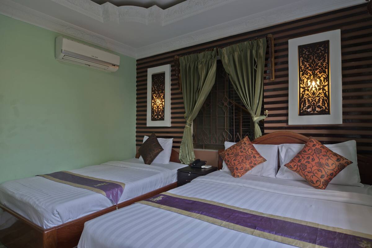 A hotel room with two single beds, a wooden headboard, a nightstand, an air conditioning unit, and decorative wall panels.