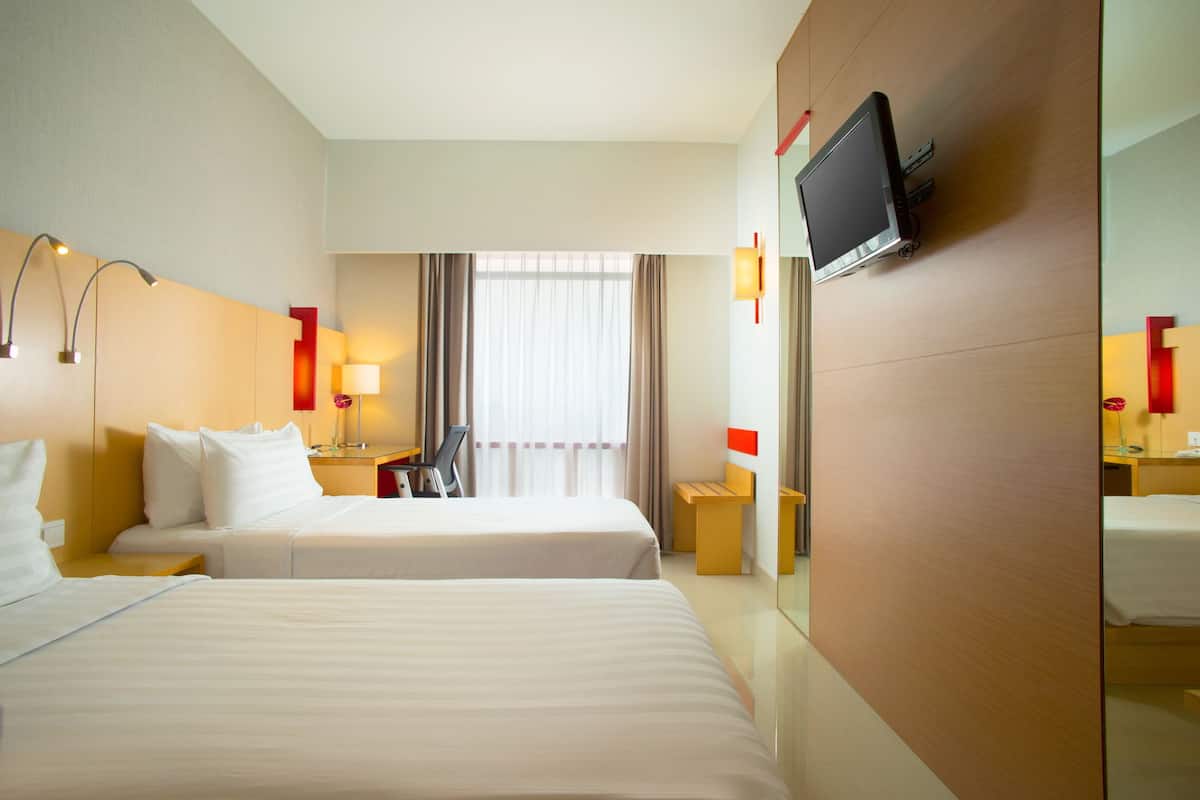 A hotel room with two beds, a TV mounted on the wall, and a window with curtains.