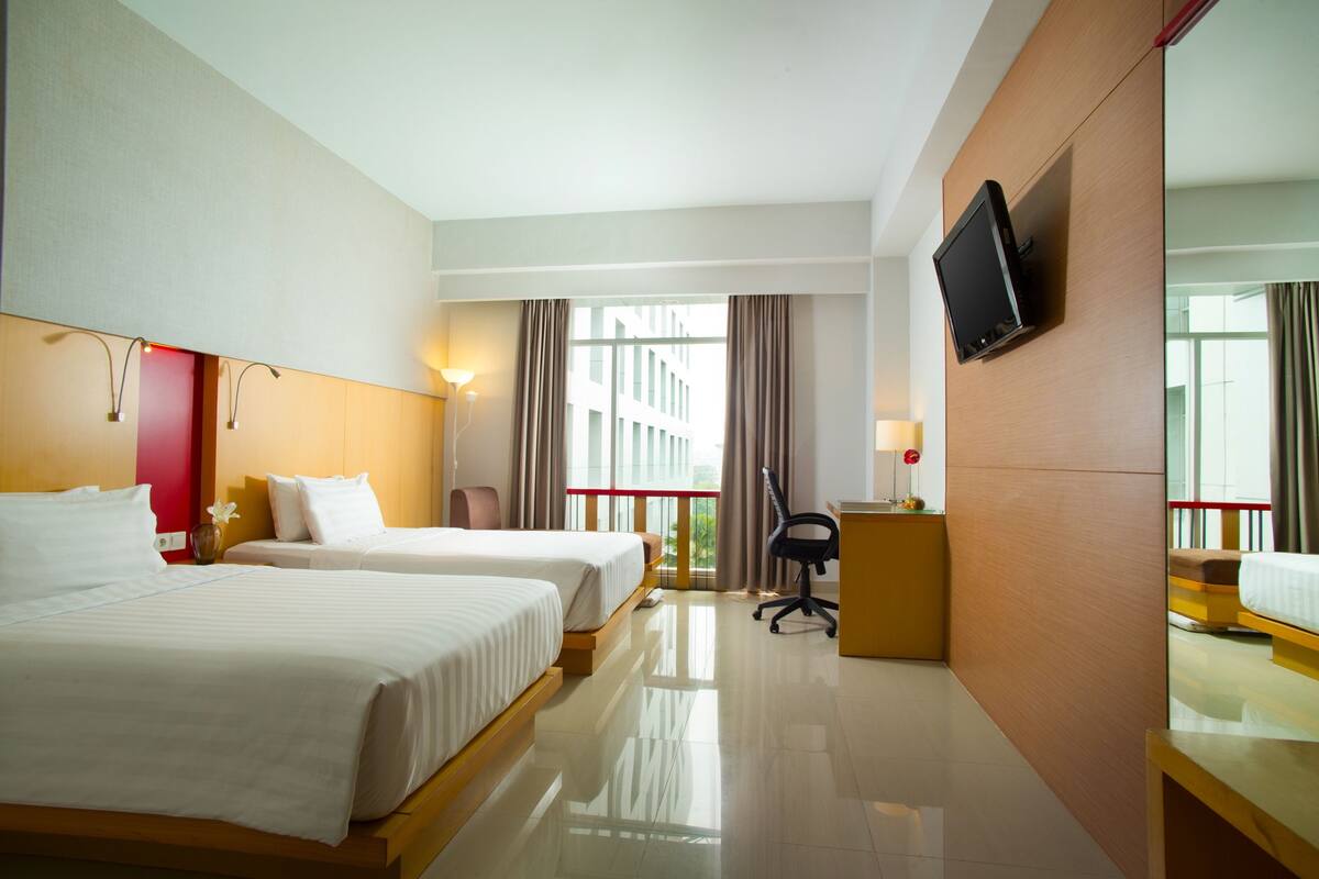 A hotel room with two beds, a TV mounted on the wall, a desk, and a chair.