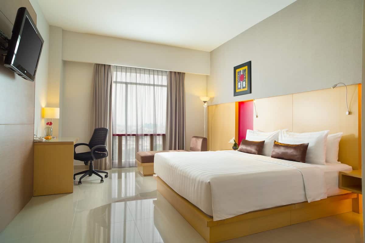 A hotel room with a large bed, a desk with a chair, a television, and a window with curtains.