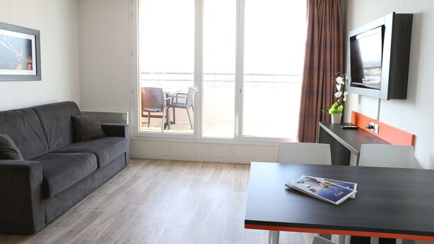 Une pièce moderne avec un canapé gris, une table à manger et un téléviseur fixé au mur.