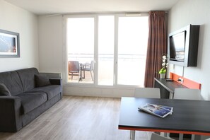 A modern room with a grey sofa, a dining table, and a TV mounted on the wall. - Adonis Paris Sud (Chevilly-Larue)