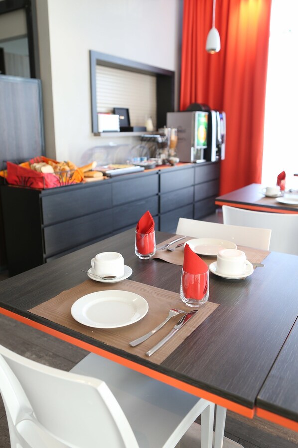 A modern dining area with a dark wooden table, white chairs, and a red curtain in the background.