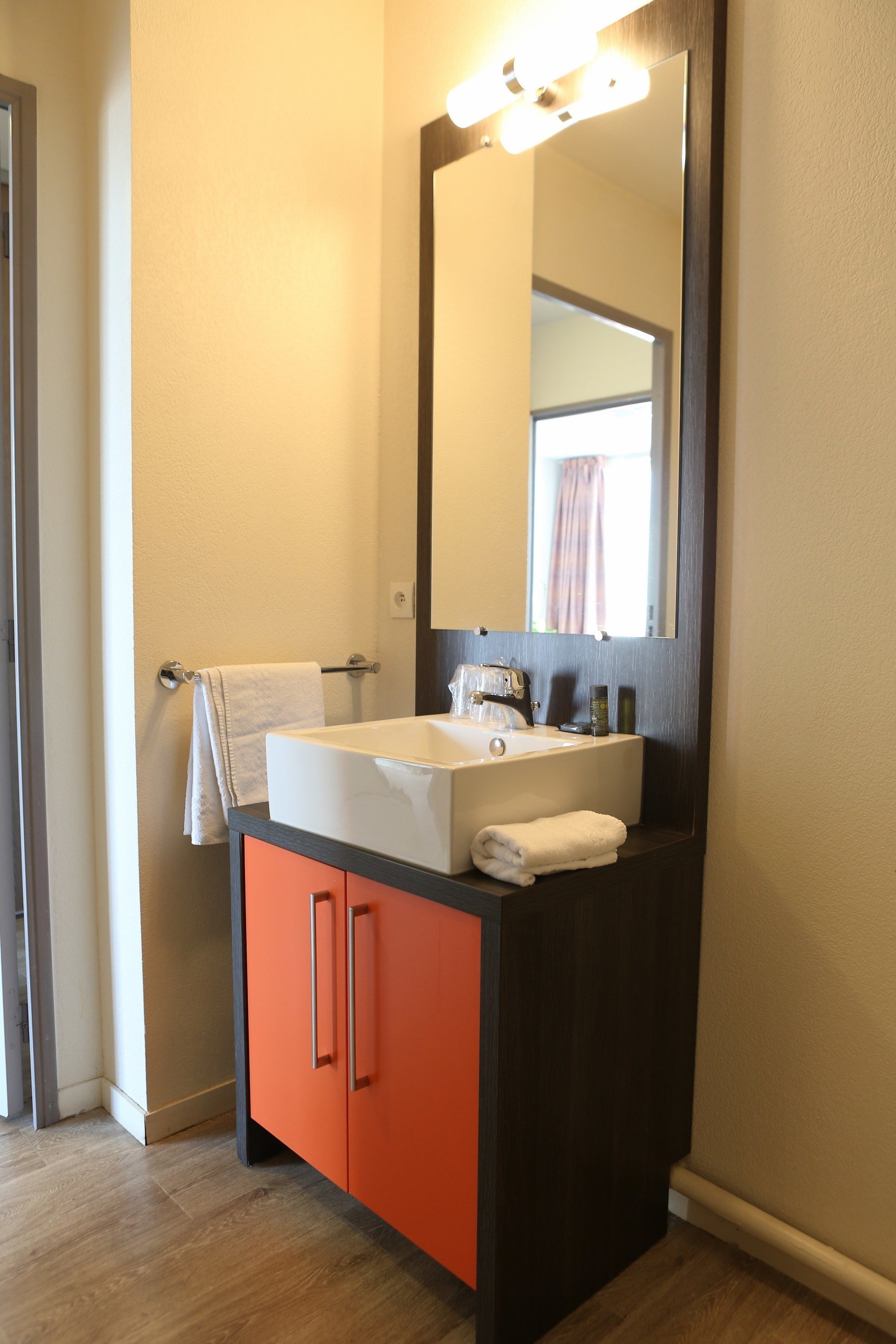 A bathroom with a white sink, orange cabinet, and a large mirror.