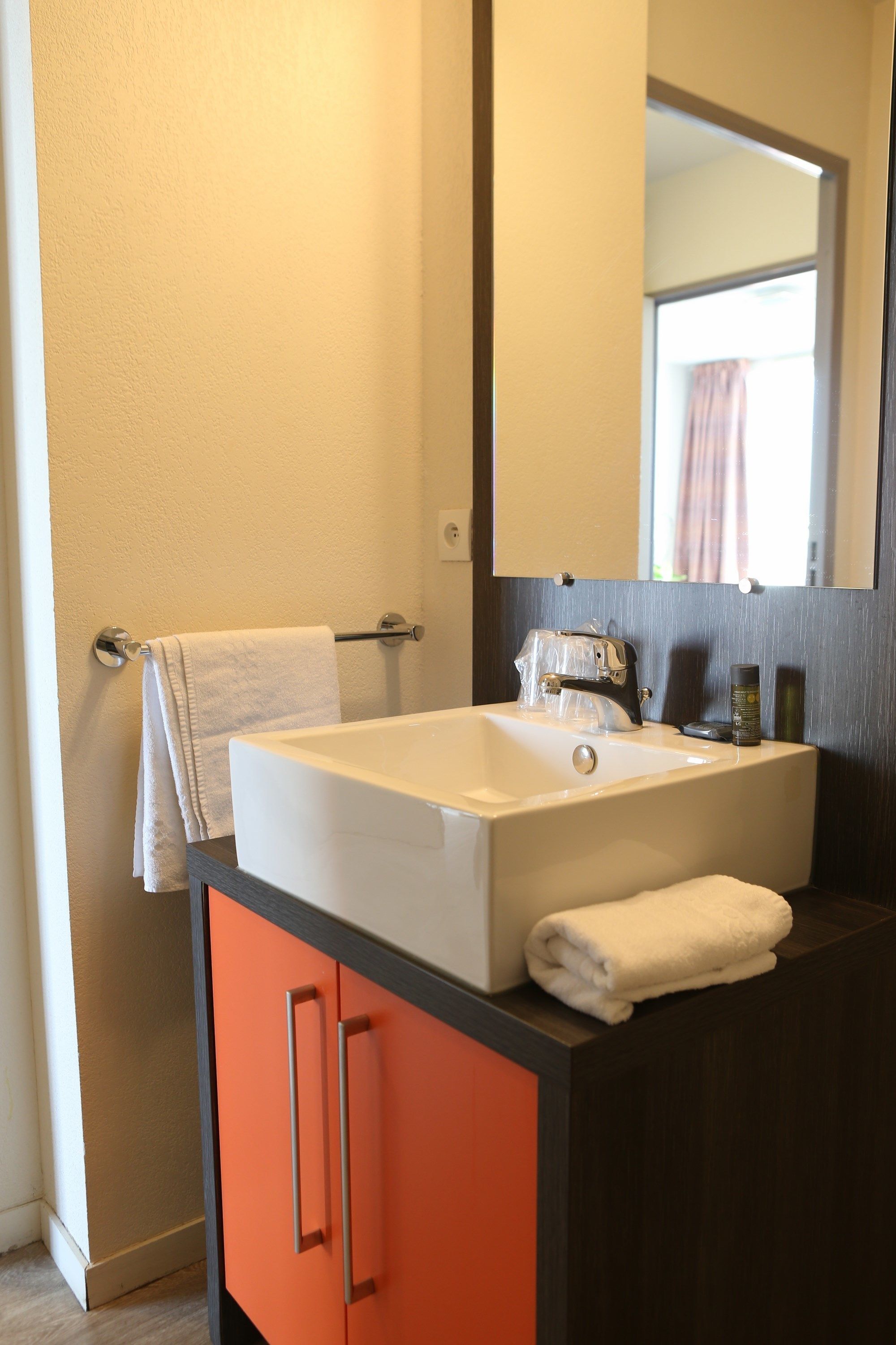 A bathroom with a white sink, a mirror above it, and an orange cabinet below.