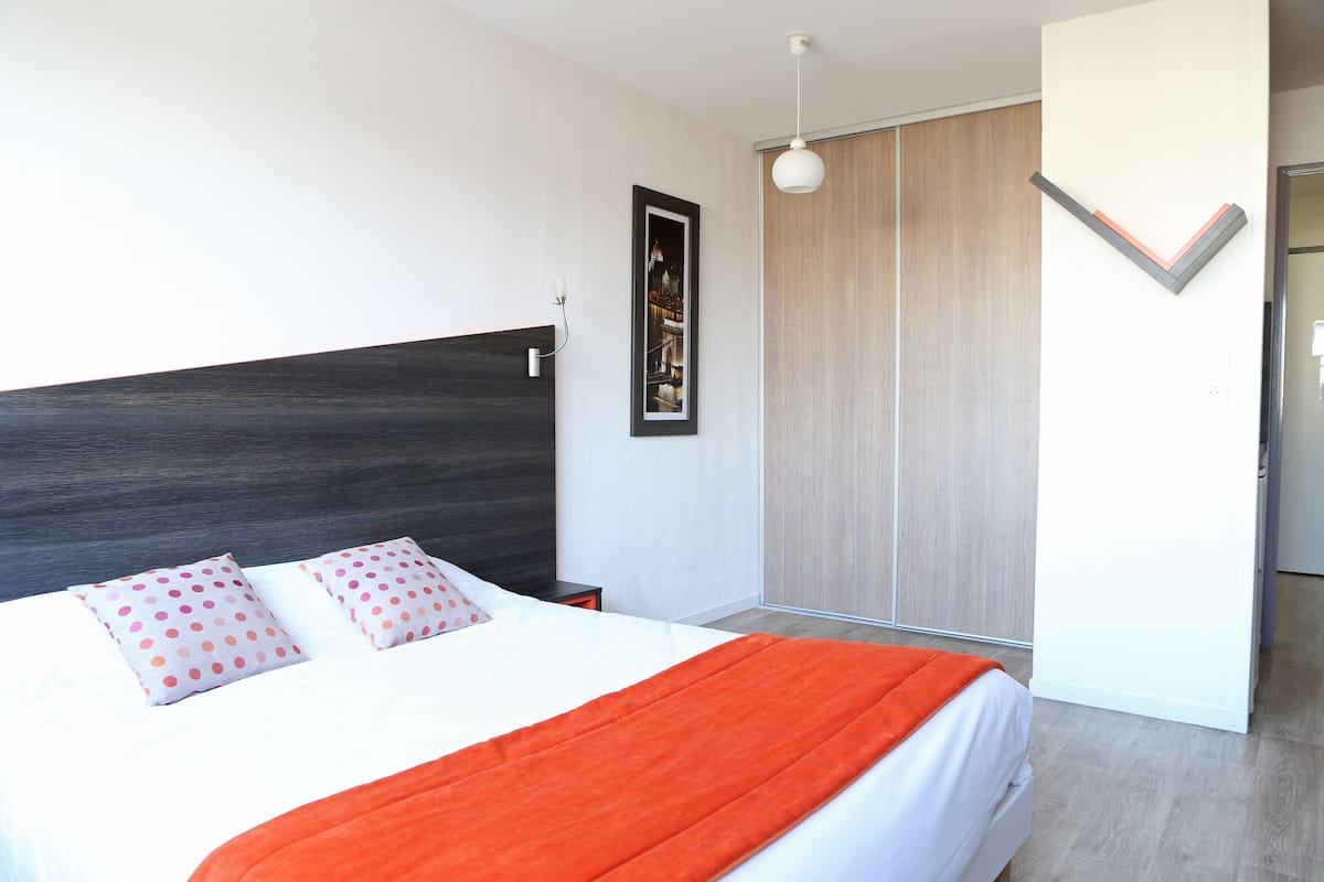 Quarto moderno com cama grande, cabeceira escura, quadro emoldurado e luminária.