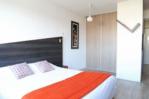 Une chambre à coucher moderne avec un grand lit, une tête de lit sombre, un tableau encadré et un luminaire.