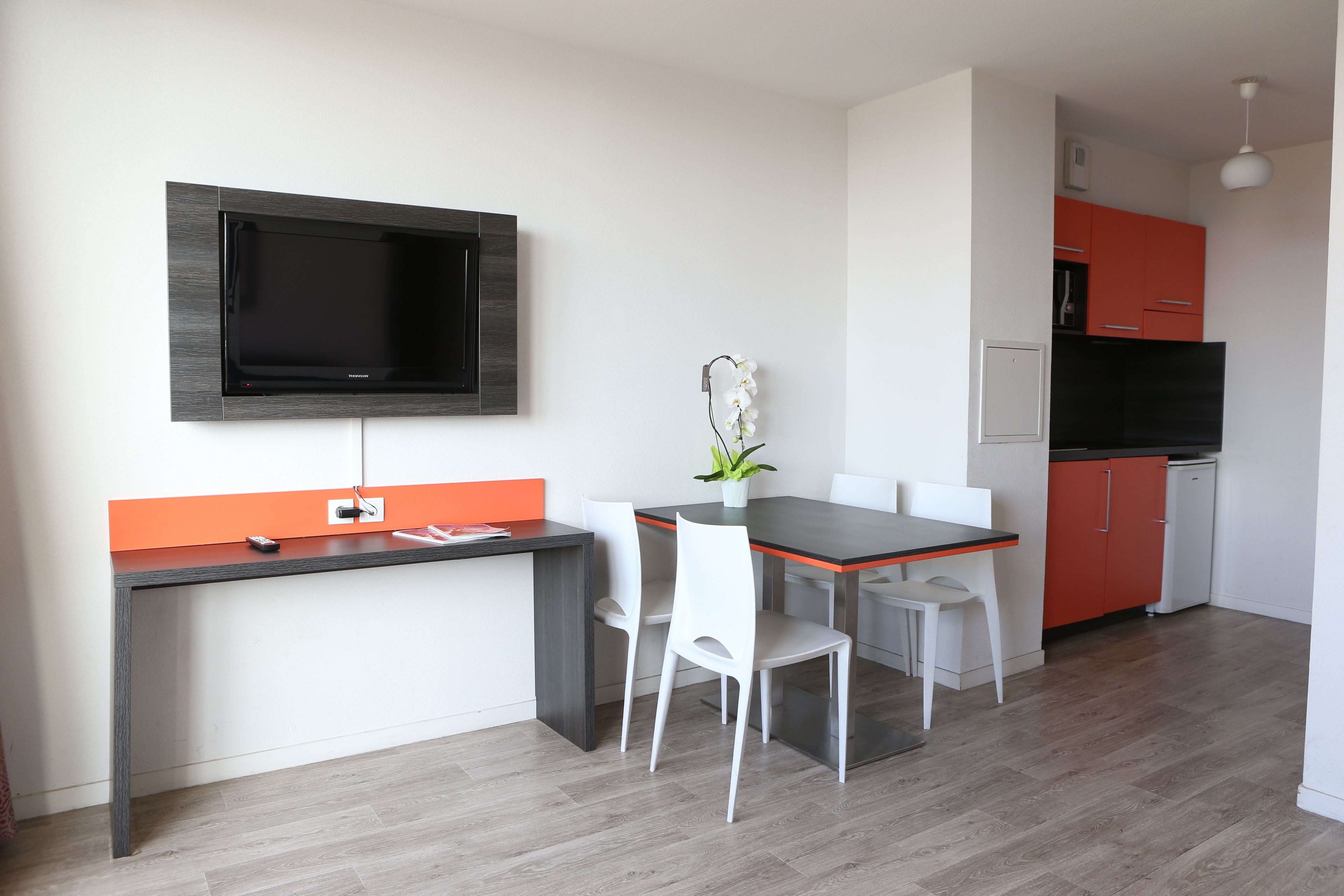 A modern kitchen with a flat-screen TV, a dining table with chairs, and a small potted plant.
