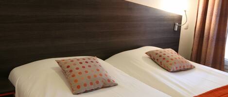 A double bed with white bedding and orange accents, a dark headboard, and a wall-mounted light fixture.