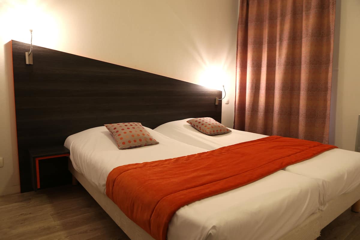 Uma cama de casal com um cobertor laranja, duas almofadas, uma cabeceira escura e uma mesinha de cabeceira.