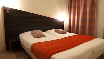 Un lit double avec une couverture orange, deux oreillers, une tête de lit sombre et une table de chevet.