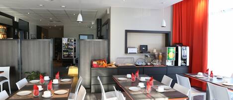 A modern dining area with tables set for service, a kitchen area with appliances, and a bright red curtain.