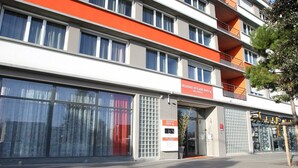 Un hôtel à plusieurs étages au design moderne, doté de grandes fenêtres et d’une façade où la couleur orange est particulièrement mise en valeur.