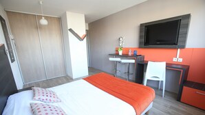 Une chambre d’hôtel moderne, dotée d’un grand lit, d’un bureau, d’une chaise et d’un téléviseur fixé au mur.