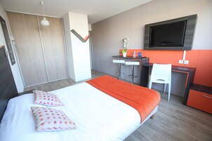 A modern hotel room with a large bed, a desk, a chair, and a TV mounted on the wall.