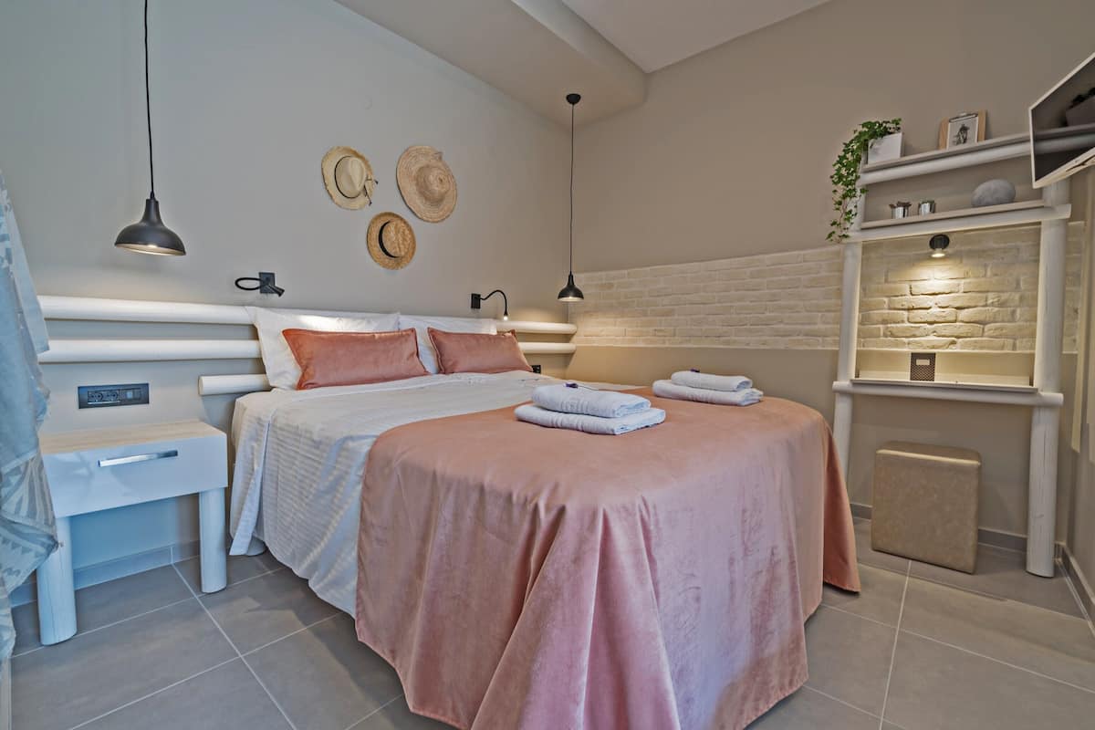 A bedroom with a bed, bedside tables, a shelf with decorative items, and a brick wall.