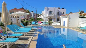 Una piscina con baldosas de mosaico azul, rodeada de sillones de descanso y sombrillas.