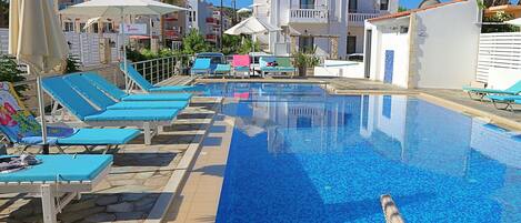 A swimming pool with blue mosaic tiles, surrounded by lounge chairs and umbrellas.