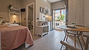 Un dormitorio moderno con cama, mesitas de noche, televisión integrada y balcón con zona de comedor.