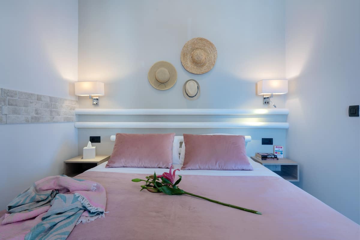 A hotel room with a bed, two nightstands, a wall-mounted hat, two wall lamps, and a bedside table with a tissue box and a clock.