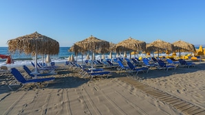Una playa con filas de sillas azules y sombrillas de paja.