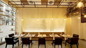 Een restaurant met een lange gedeelde tafel, meerdere zitjes en zwarte stoelen.