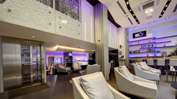 Een moderne hotellobby met een receptiebalie, zithoek en een bar.
