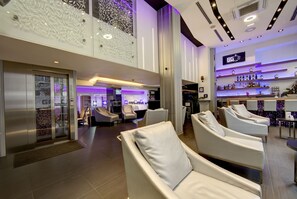 Un hall d’hôtel moderne comprenant un comptoir d’accueil, un espace salon et un bar.