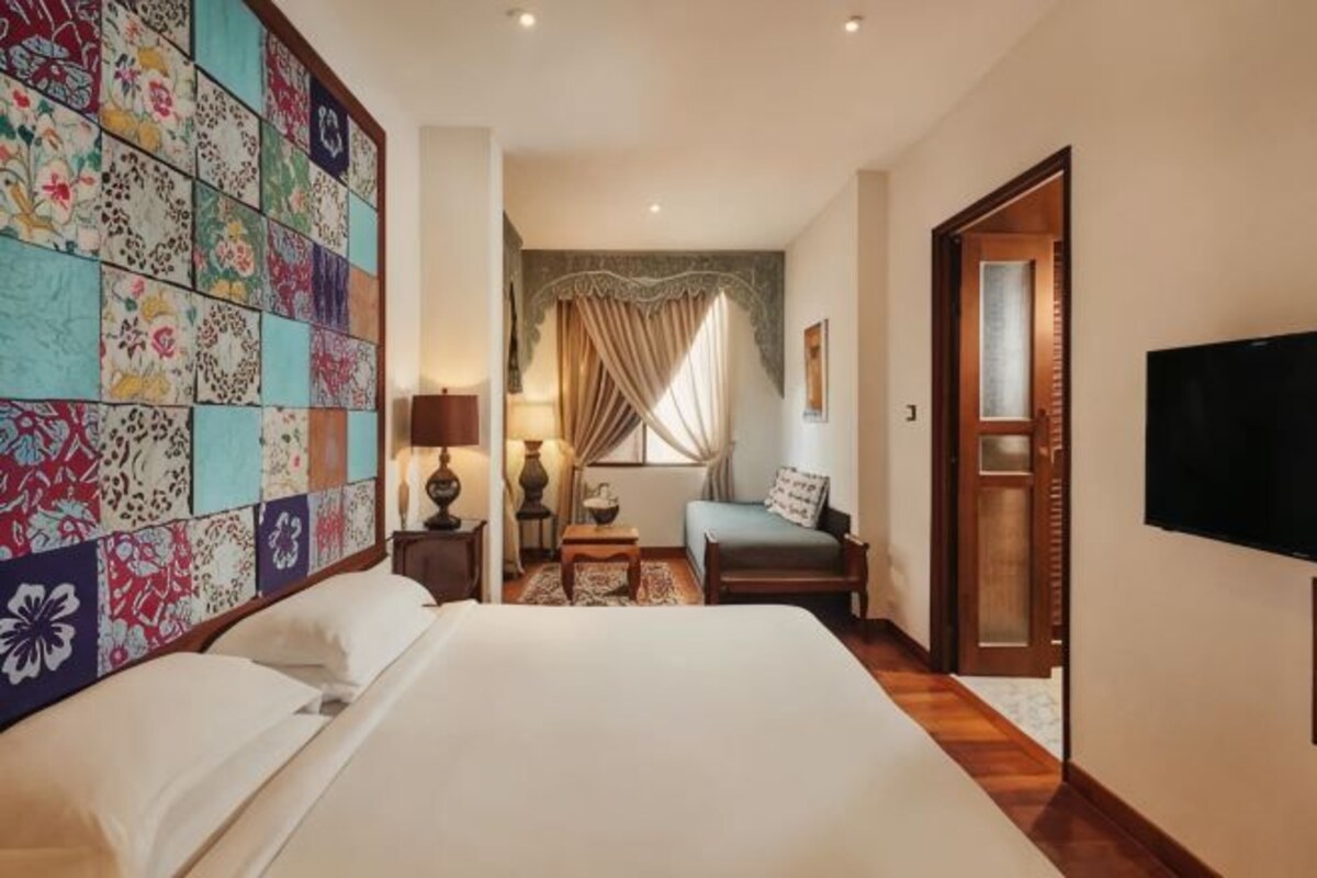 Une chambre d’hôtel avec un grand lit, un téléviseur fixé au mur, un plancher en bois et une décoration murale colorée.