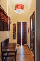 Un pasillo con un banco de madera, una lámpara colgante de diseño rojo y una puerta al final.