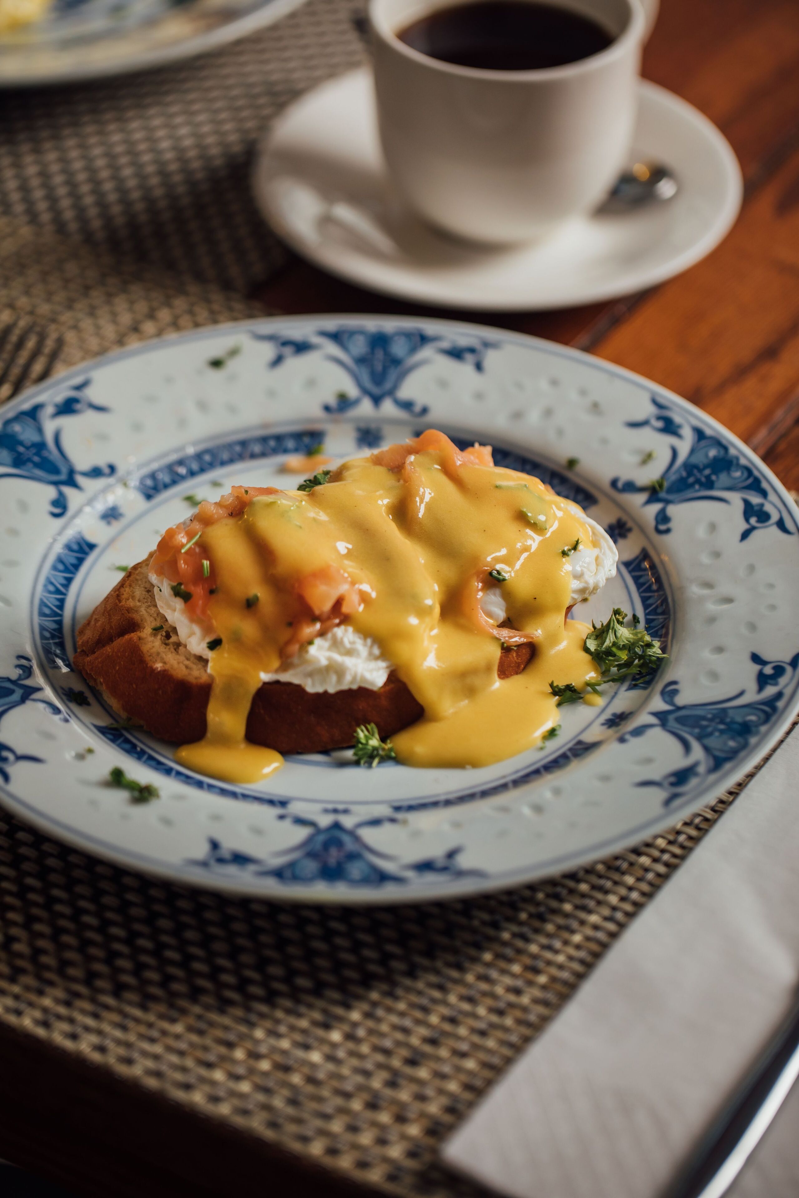 A breakfast plate with eggs benedict and a cup of coffee on a table.