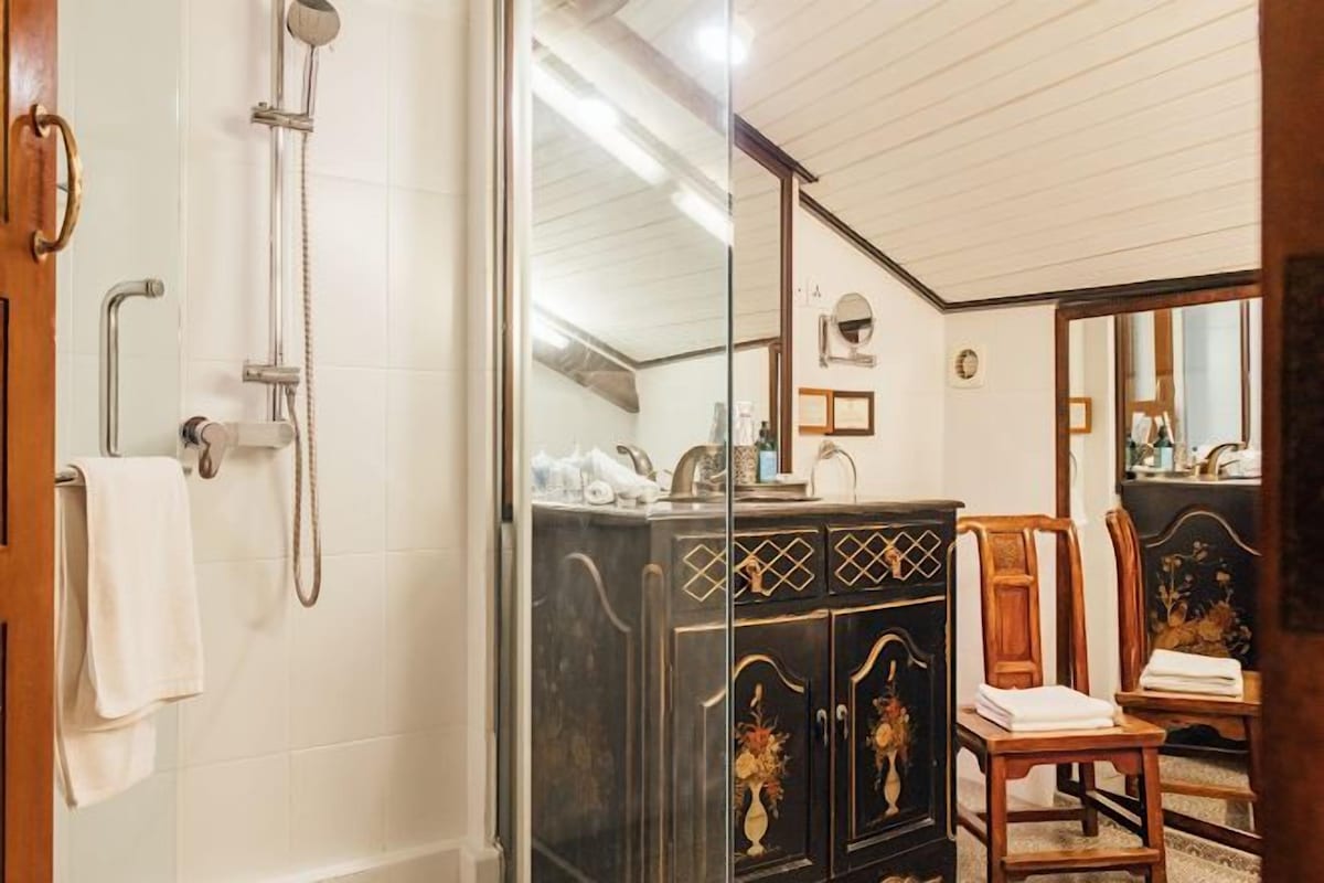 A bathroom with a glass-enclosed shower, a wooden cabinet with decorative carvings, and a mirror reflecting the room.
