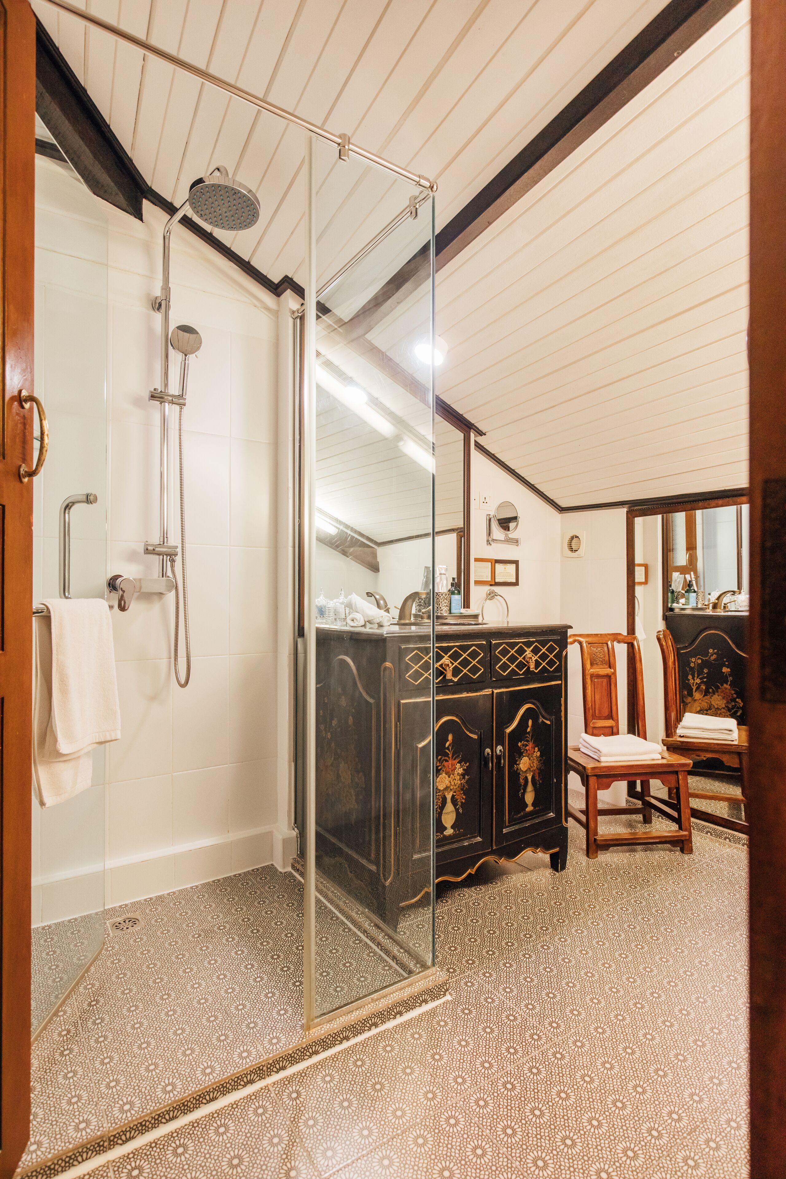 Een badkamer met een douchecabine van glas, een houten wastafelmeubel met sierlijk houtsnijwerk en een vloer met een patroon.