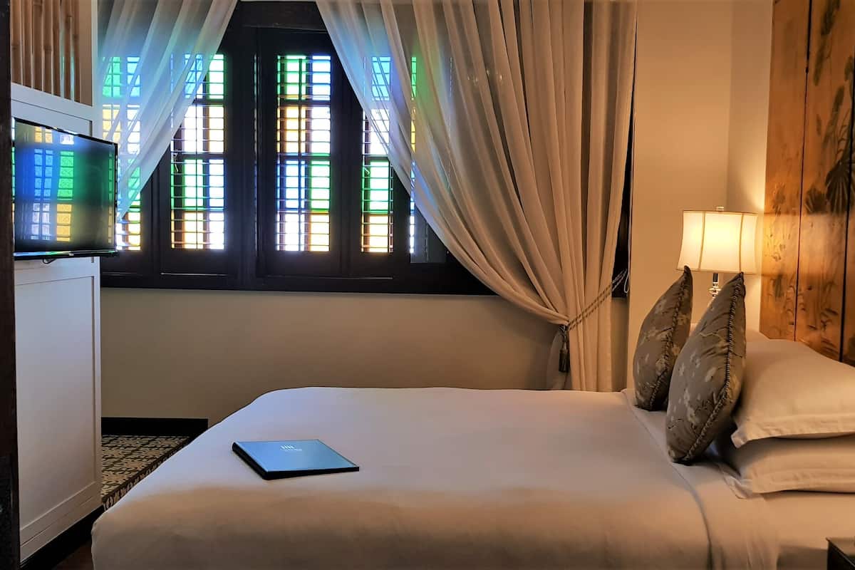 A hotel room with a bed, a desk with a laptop, a lamp, and a window with curtains.