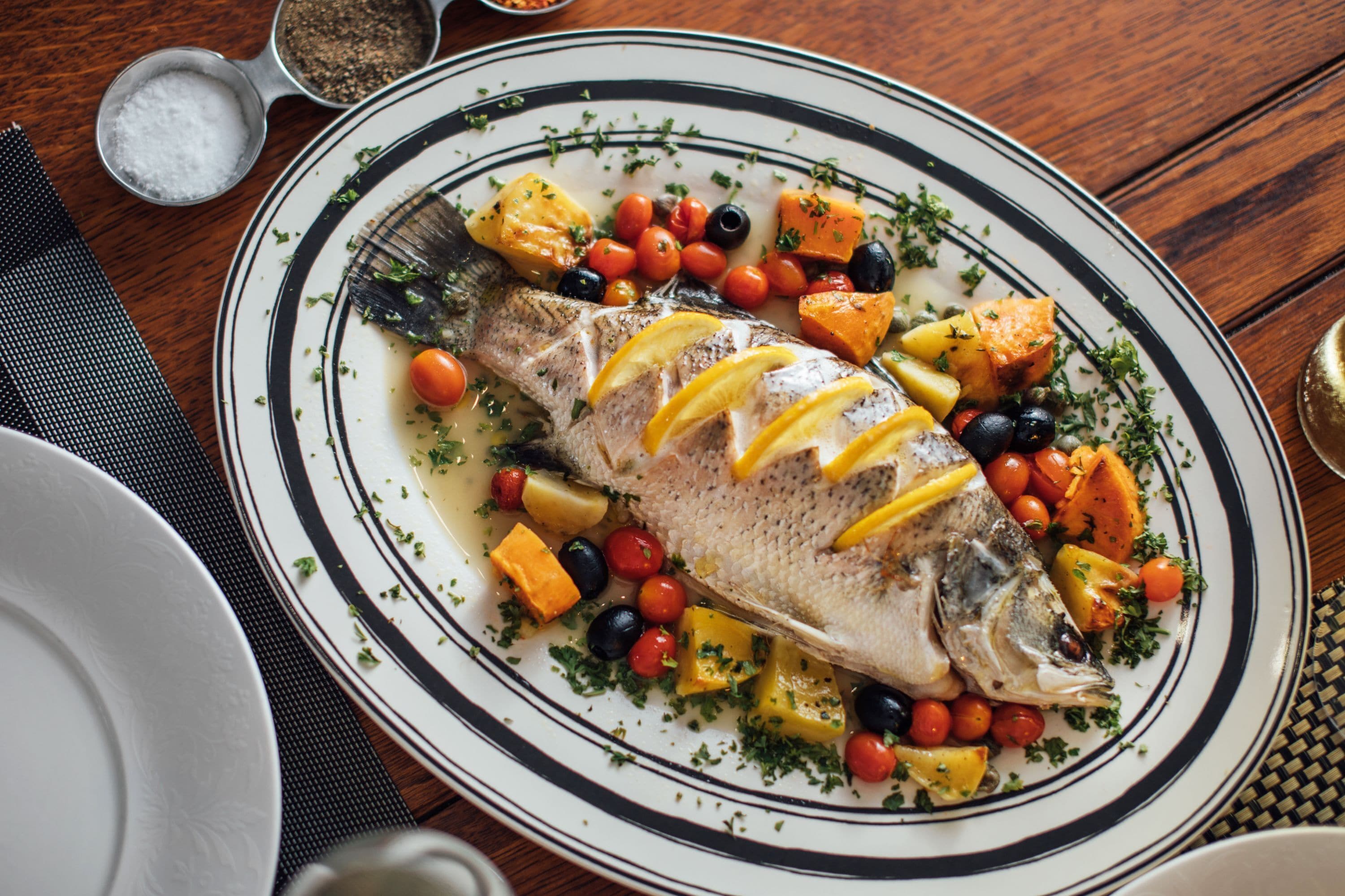 A plate of roasted fish with lemon slices, cherry tomatoes, and herbs.