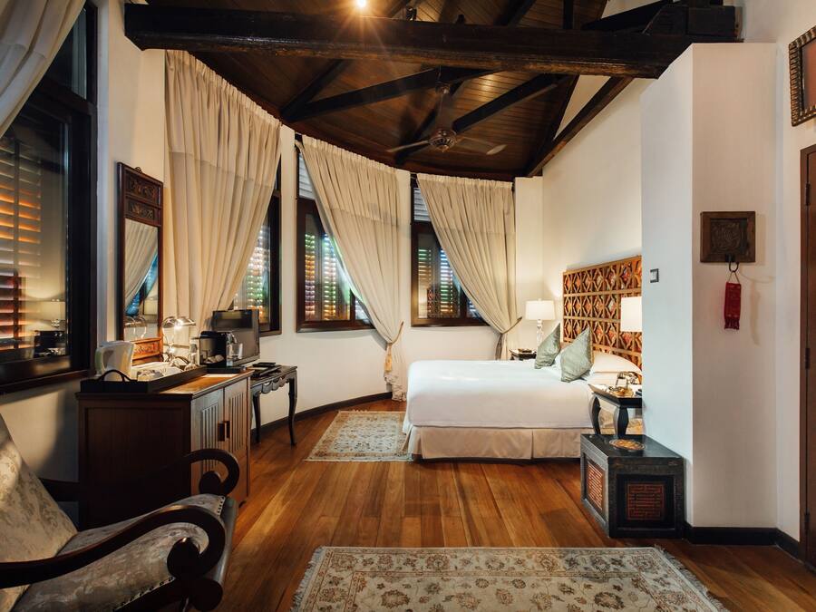A bedroom with a wooden ceiling, a bed, a desk, a chair, and a nightstand.