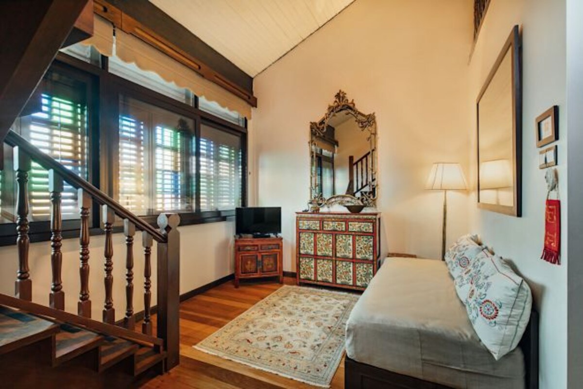 Une pièce chaleureuse avec un escalier en bois, un téléviseur posé sur un meuble en bois, un tapis à motifs et un lit agrémenté d’un coussin décoratif.