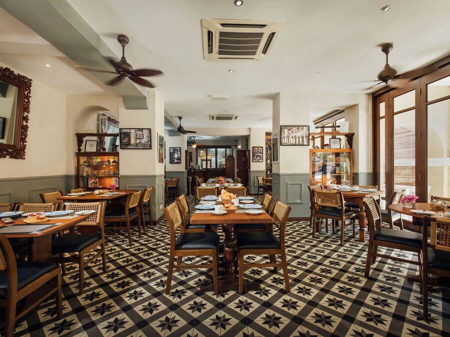 A dining area with multiple tables and chairs, a patterned floor, ceiling fans, and framed pictures on the walls.