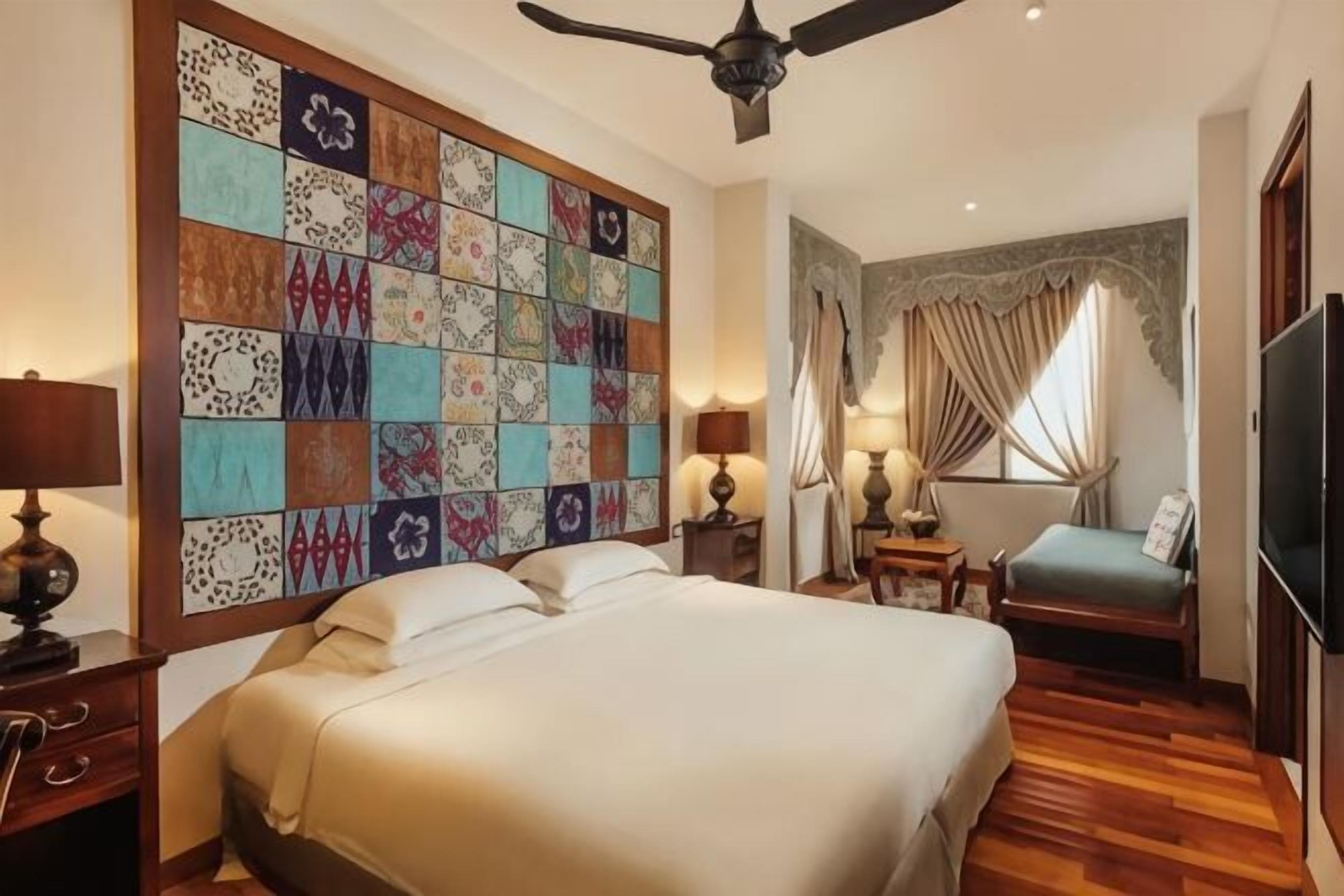A hotel room with a large bed, a ceiling fan, a television, a desk with a lamp, and a decorative wall panel.