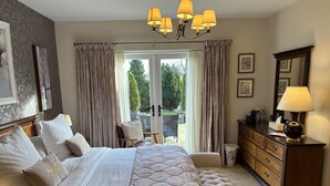 Une chambre élégamment aménagée, dotée d’un grand lit, d’une commode, d’un fauteuil près de la fenêtre et d’un lustre.