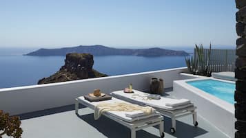 A sunlit terrace with two sunbeds, a small table with a hat and candles, and a stone wall.